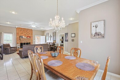 Tiled dining room with brick wall, a fireplace, ceiling fan with notable chandelier, and crown molding