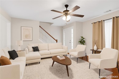 Living area with a ceiling fan, wood finished floors, and stairway