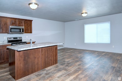 Kitchen featuring appliances with stainless steel finishes, a center island with sink, open floor plan, and dark wood-style flooring