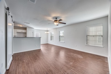 Unfurnished living room featuring a barn door, dark wood-style floors, ceiling fan, and a chandelier