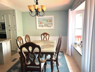 Dining room with light tile patterned floors, a chandelier, a textured ceiling, and a wainscoted wall