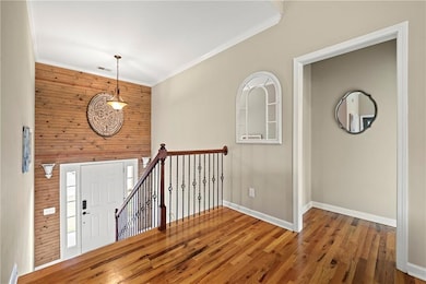Entrance foyer with baseboards, wooden walls, ornamental molding, and wood finished floors