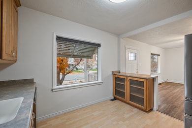 Kitchen open to living room featuring brown cabinets, a textured ceiling, dark countertops, light wood-style flooring, and glass insert cabinets