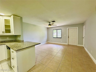 Kitchen with kitchen peninsula, light tile patterned floors, white cabinetry, and light stone counters