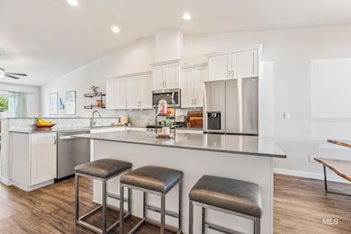 Kitchen with a breakfast bar, appliances with stainless steel finishes, white cabinetry, vaulted ceiling, and dark wood-type flooring