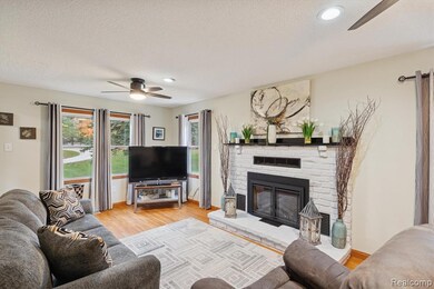 Living area featuring a ceiling fan, light wood-style floors, a brick fireplace, and a textured ceiling
