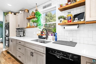 Kitchen featuring open shelves, dishwasher, a sink, decorative backsplash, and light countertops