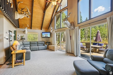 Carpeted living room with high vaulted ceiling, a wooden ceiling with exposed beams, and ceiling fan