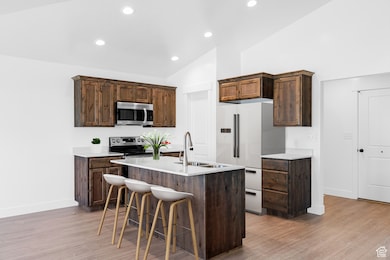 Kitchen featuring appliances with stainless steel finishes, vaulted ceiling, light wood-type flooring, a kitchen breakfast bar, and light countertops