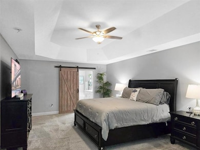 Bedroom with a barn door, ceiling fan, a tray ceil