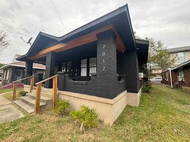 View of property exterior with brick siding, a lawn, and covered porch