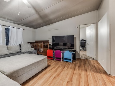 Living area featuring wood finished floors, lofted ceiling, a ceiling fan, and a textured ceiling