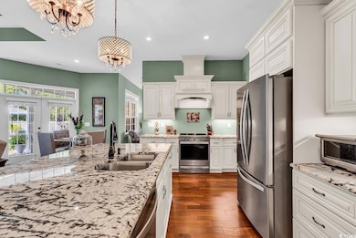 Kitchen featuring stainless steel appliances, a sink, a chandelier, white cabinets, and dark wood finished floors
