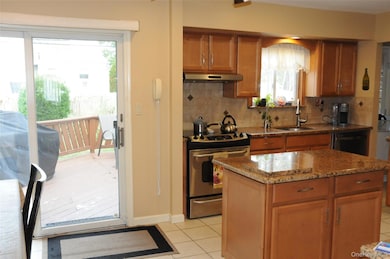 Kitchen featuring brown cabinetry, stainless steel electric range oven, light tile patterned floors, backsplash, and light stone countertops