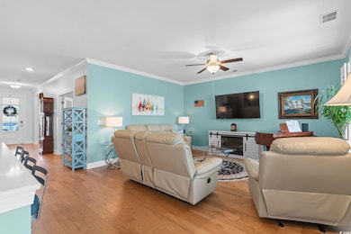 Living room with light wood finished floors, a glass covered fireplace, ornamental molding, and ceiling fan