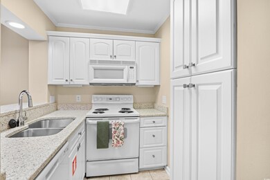Kitchen with white appliances, white cabinetry, light stone counters, light tile patterned flooring, and ornamental molding