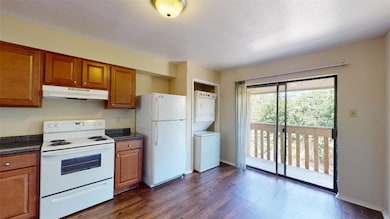 Kitchen with white appliances, brown cabinetry, dark wood-style floors, and under cabinet range hood