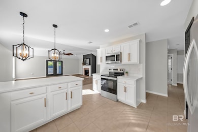 Kitchen featuring appliances with stainless steel finishes, tasteful backsplash, a fireplace, white cabinetry, and decorative light fixtures