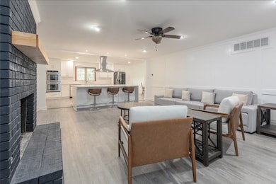 Living area featuring light wood-style floors, ceiling fan, a brick fireplace, and a decorative wall