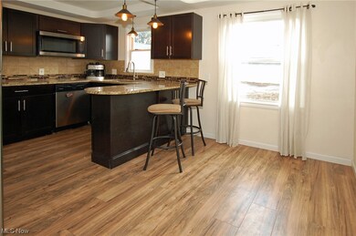 Kitchen with hanging light fixtures, light stone countertops, stainless steel appliances, backsplash, and light wood-style flooring