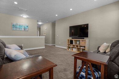 Living area featuring a textured ceiling, visible vents, carpet floors, baseboards, and recessed lighting
