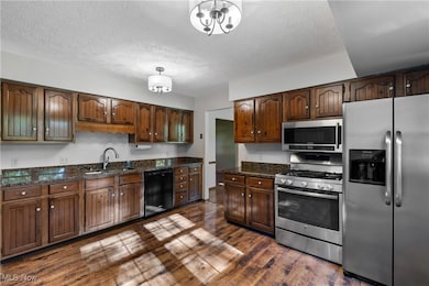 Kitchen with appliances with stainless steel finishes, dark wood-type flooring, dark stone countertops, a textured ceiling, and pendant lighting
