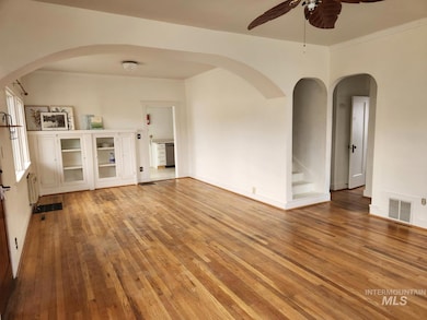 Unfurnished room with arched walkwayDs, light wood-style flooring, crown molding, a ceiling fan, and stairway