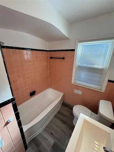 Bathroom featuring dark wood-type flooring, tile walls, a wainscoted wall, and shower / washtub combination