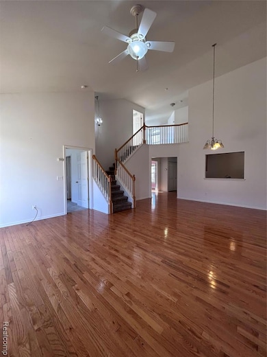 Unfurnished living room featuring high vaulted ceiling, stairs, wood finished floors, a ceiling fan, and a chandelier