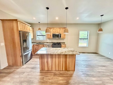 Kitchen with light brown cabinets, appliances with stainless steel finishes, light wood-style flooring, a center island, and recessed lighting