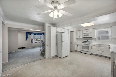 Kitchen with white appliances, light carpet, light countertops, white cabinetry, and light floors