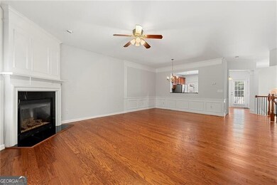 Living room with a ceiling fan, a fireplace, a chandelier, a decorative wall, and light wood-style floors