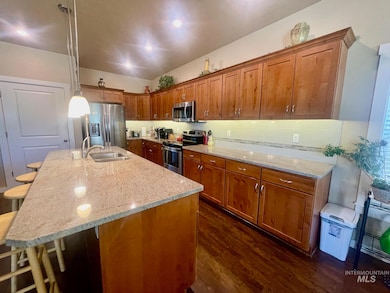 Kitchen featuring stainless steel appliances, dark wood finished floors, brown cabinets, and light stone countertops