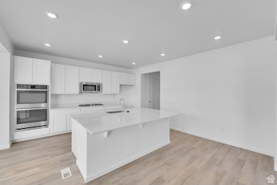 Kitchen featuring appliances with stainless steel finishes, a sink, recessed lighting, white cabinets, and light wood-type flooring