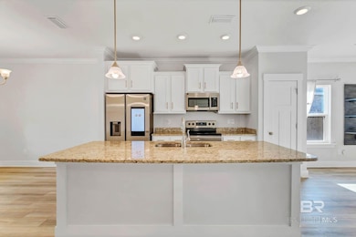 Kitchen featuring ornamental molding, stainless steel appliances, white cabinets, light stone countertops, and light wood-type flooring