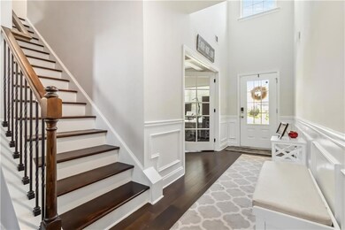 Entryway with stairs, a wainscoted wall, dark wood-type flooring, a decorative wall, and a high ceiling