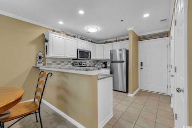 Kitchen with decorative backsplash, appliances with stainless steel finishes, white cabinets, and crown molding
