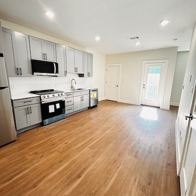 Kitchen featuring gray cabinetry, light countertops, stainless steel appliances, decorative backsplash, and light wood-type flooring
