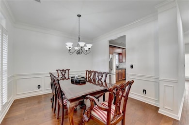 Dining room featuring crown molding, a chandelier, a decorative wall, light wood finished floors, and wainscoting