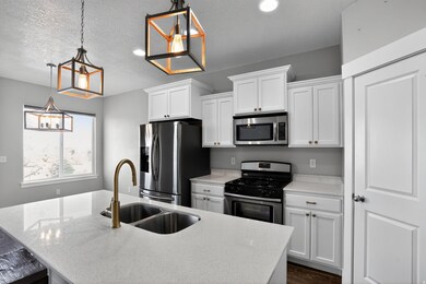 Kitchen with stainless steel appliances, decorative light fixtures, white cabinetry, an island with sink, and a textured ceiling