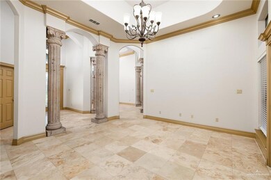 Empty room featuring decorative columns, a raised ceiling, a notable chandelier, light tile floors, and crown molding