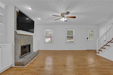 Unfurnished living room featuring ceiling fan, a stone fireplace, a textured ceiling, and light hardwood / wood-style flooring