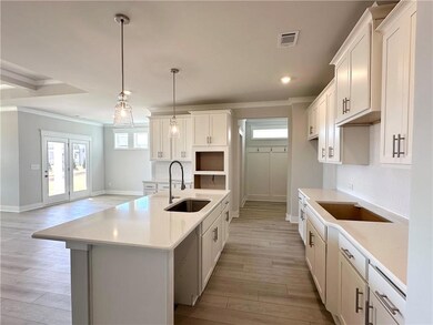 Kitchen featuring crown molding, a kitchen island with sink, hanging light fixtures, light wood finished floors, and white cabinetry
