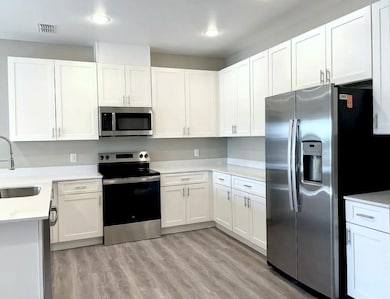 Kitchen with stainless steel appliances, white cabinets, light wood finished floors, and light stone counters