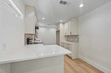 Kitchen featuring white cabinetry, light wood-style flooring, light stone counters, backsplash, and electric range oven
