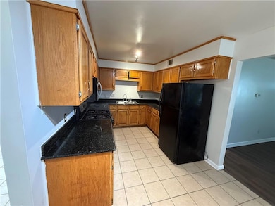 Kitchen with brown cabinets, freestanding refrigerator, light tile patterned floors, ornamental molding, and dark stone countertops