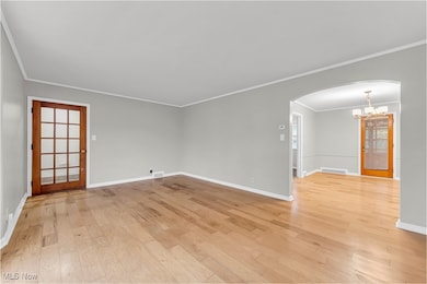 Empty room with arched walkways, ornamental molding, a chandelier, and light wood-style floors
