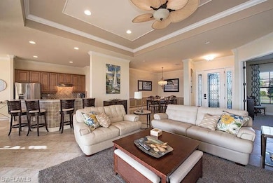 Living area featuring a raised ceiling, recessed lighting, crown molding, light tile patterned floors, and a ceiling fan