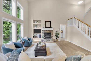 Living room featuring a towering ceiling, carpet, stairway, a stone fireplace, and built in shelves