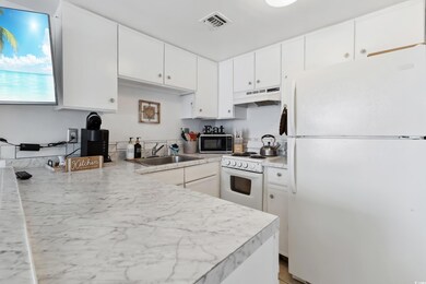 Kitchen with white appliances, under cabinet range hood, white cabinetry, and light countertops